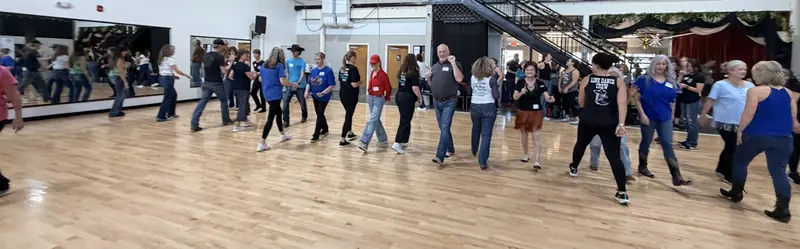 A long line of dancers moving together across a wooden floor