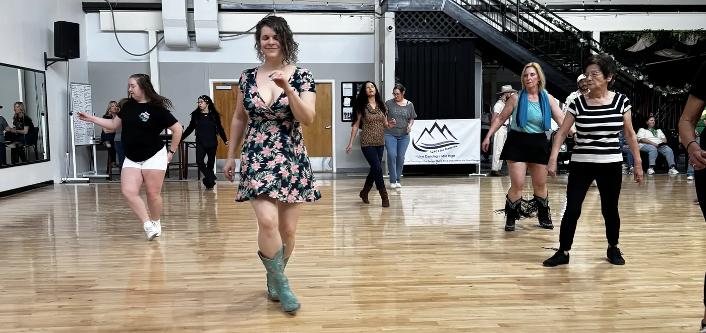 Dancers in a line stepping in unison across a bright wooden floor