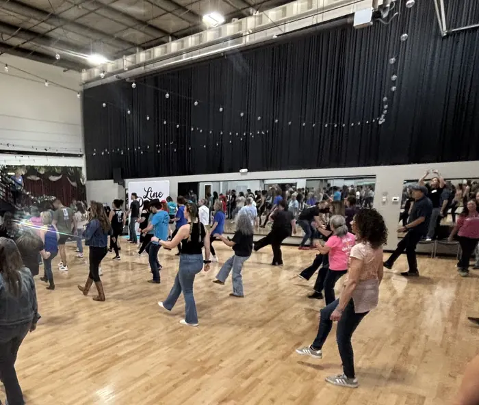 A wide ballroom filled with line dancers under string lights