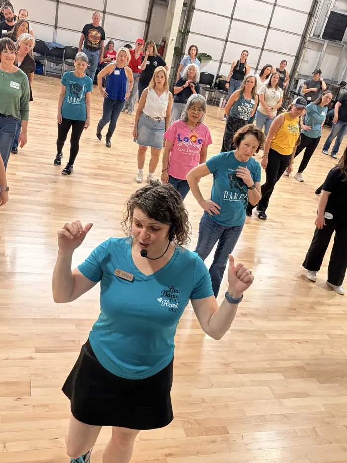 Erika teaching a line dance at the front of a full class, headset mic on